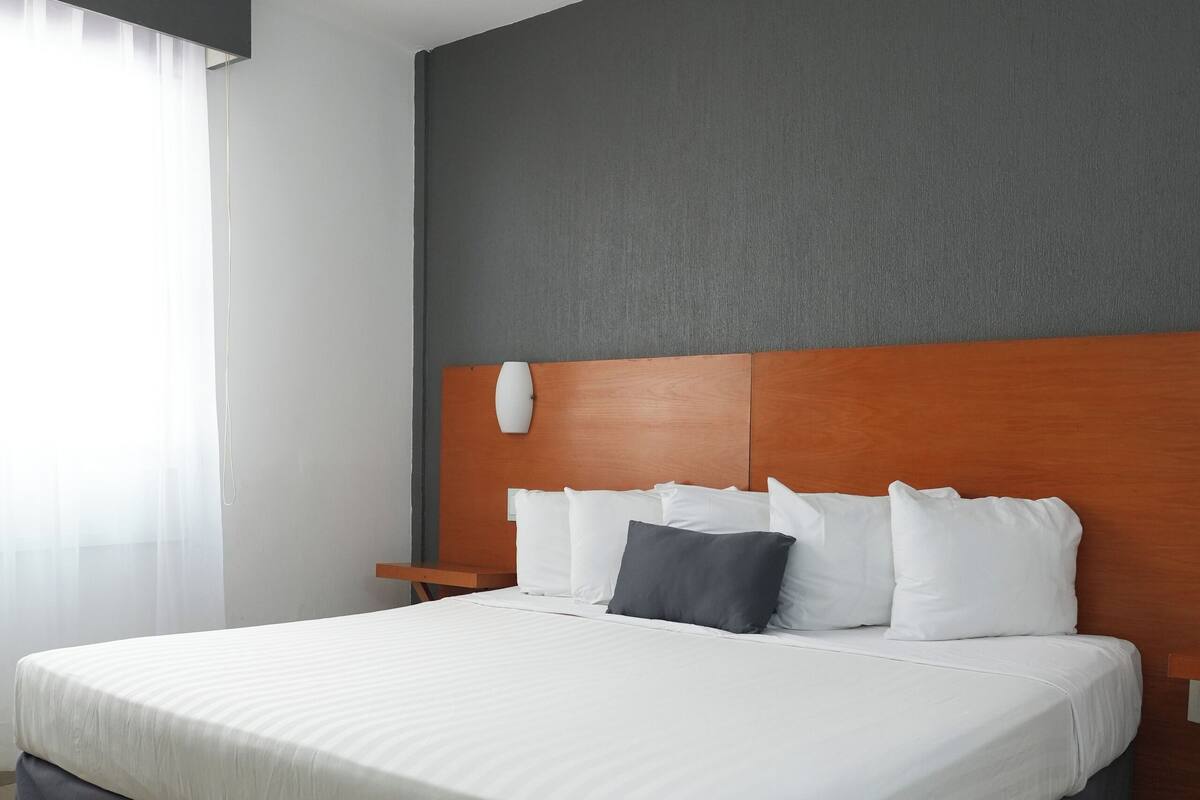 Una habitación de hotel moderna con una cama grande, un cabecero de madera y una mesita de noche.