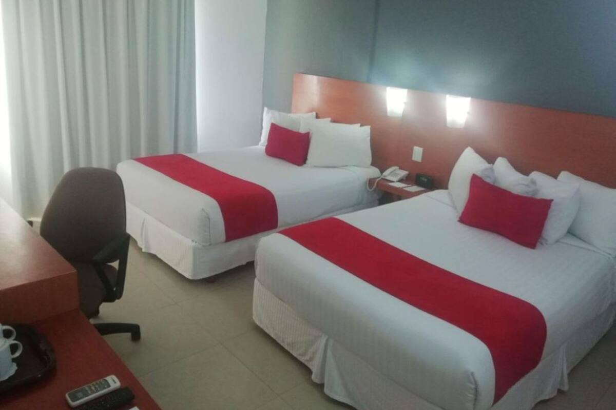 Habitación de hotel con dos camas, un escritorio, una silla y un teléfono.