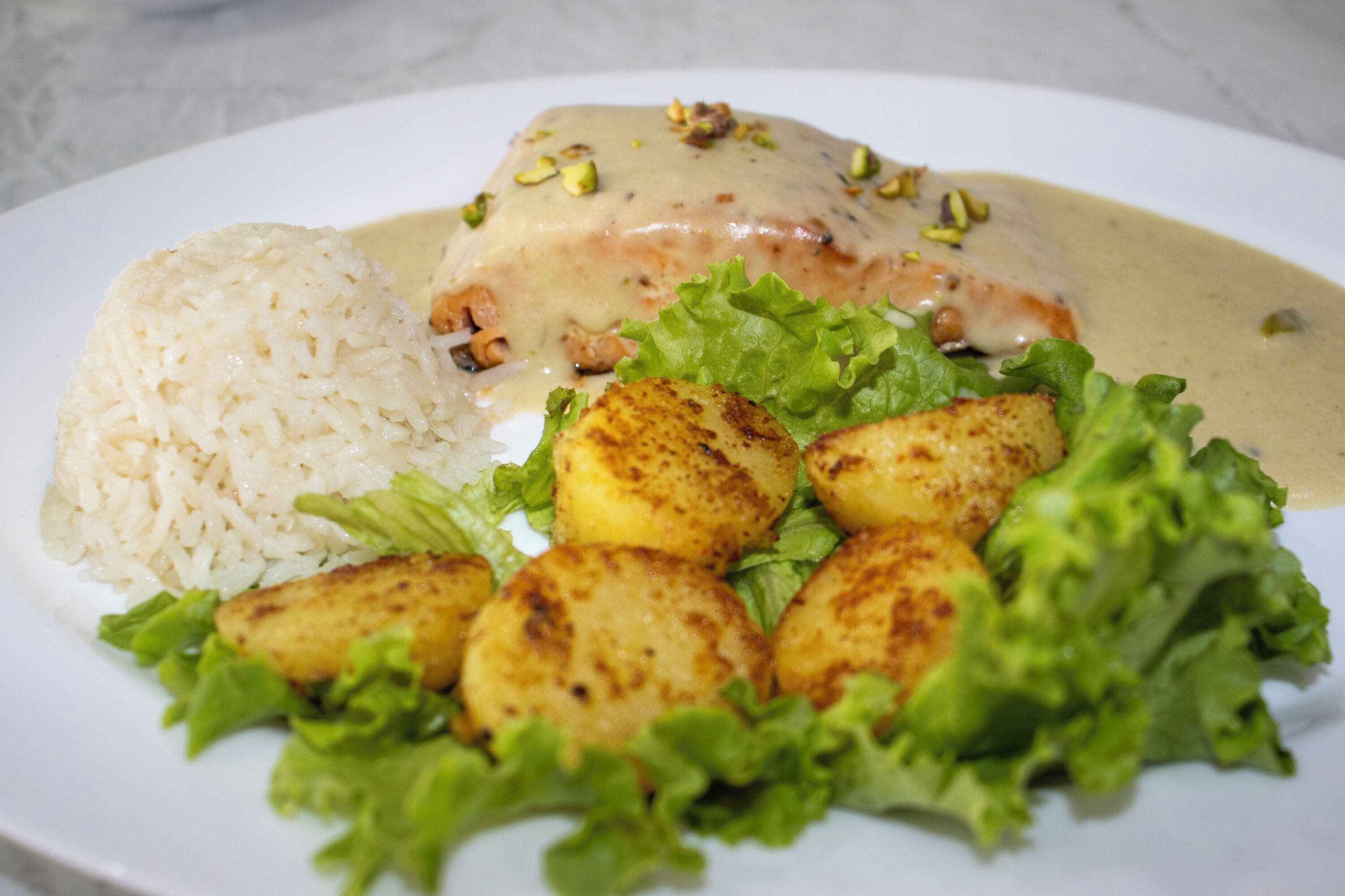 A plate with rice, a piece of meat with sauce, and roasted potatoes.