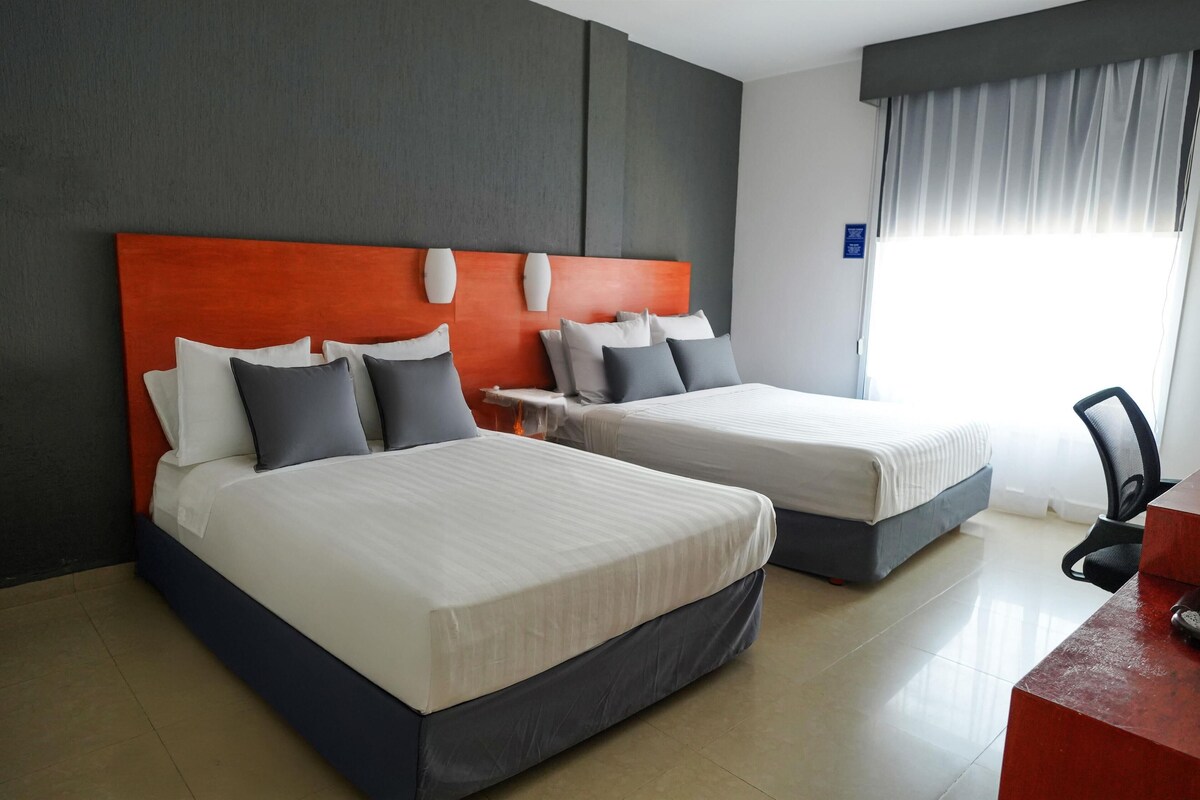 Habitación de hotel con dos camas, un escritorio y una silla.