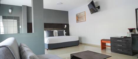 A modern hotel room with a bed, a sofa, a coffee table, a dresser, and a TV mounted on the wall.