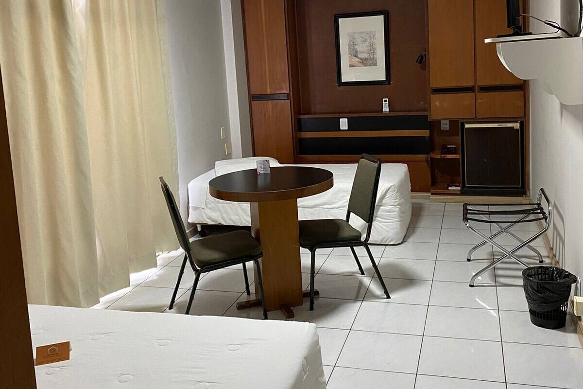 A hotel room with a bed, a small round table with two chairs, a television, and a wall-mounted shelf.