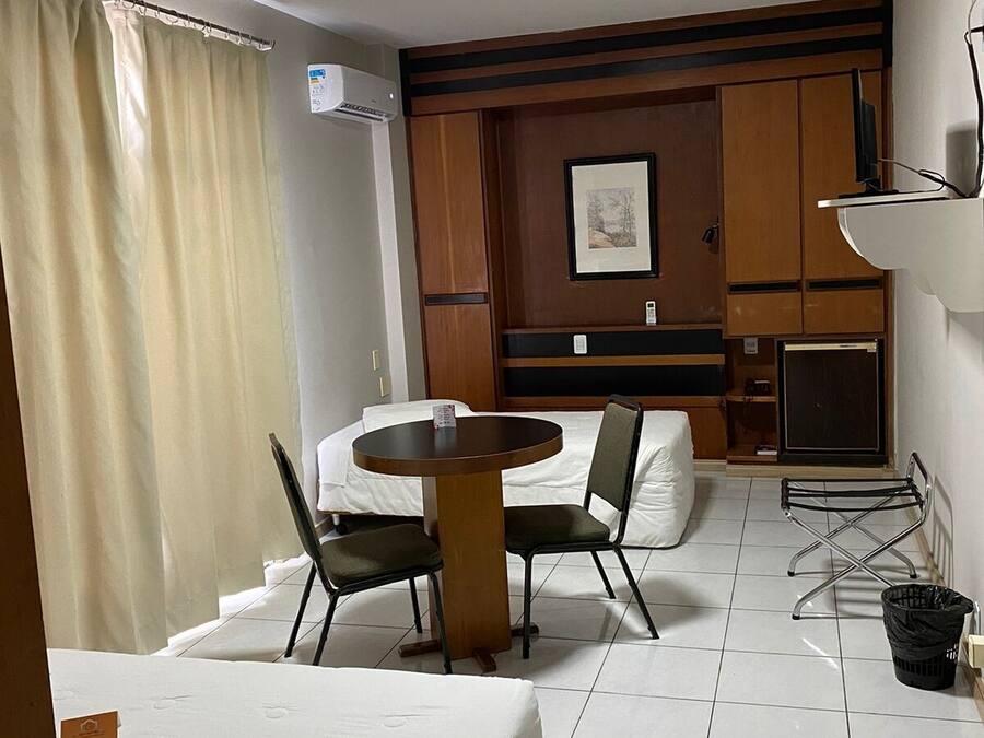 Habitació d'hotel amb un llit, una taula rodona petita amb dues cadires, una televisió i una estant penjada a la paret.
