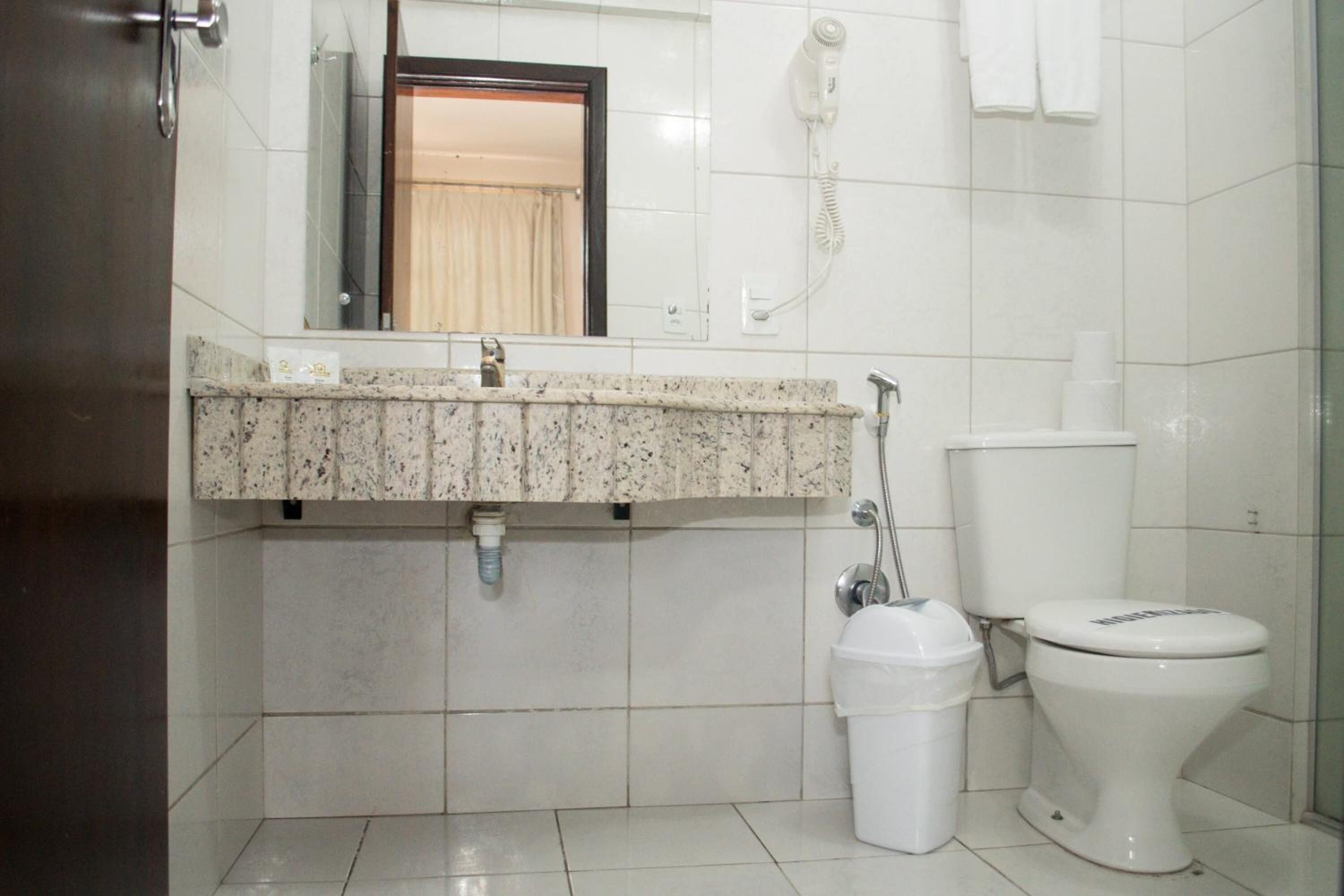 A bathroom with a granite countertop, a toilet, a trash bin, and a hand dryer.
