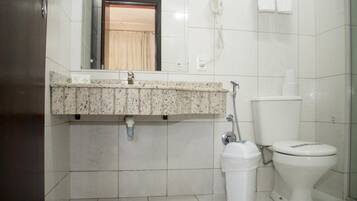 A bathroom with a granite countertop, a toilet, a trash bin, and a hand dryer.