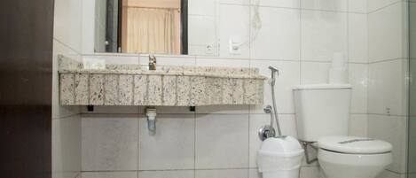 A bathroom with a granite countertop, a toilet, a trash bin, and a hand dryer.