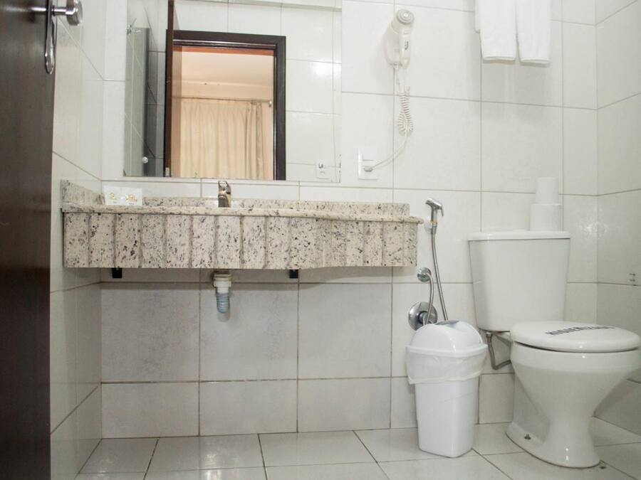 A bathroom with a granite countertop, a toilet, a trash bin, and a hand dryer.