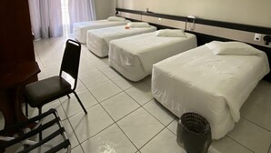 A hotel room with three single beds, a chair, a trash bin, and a window with curtains.