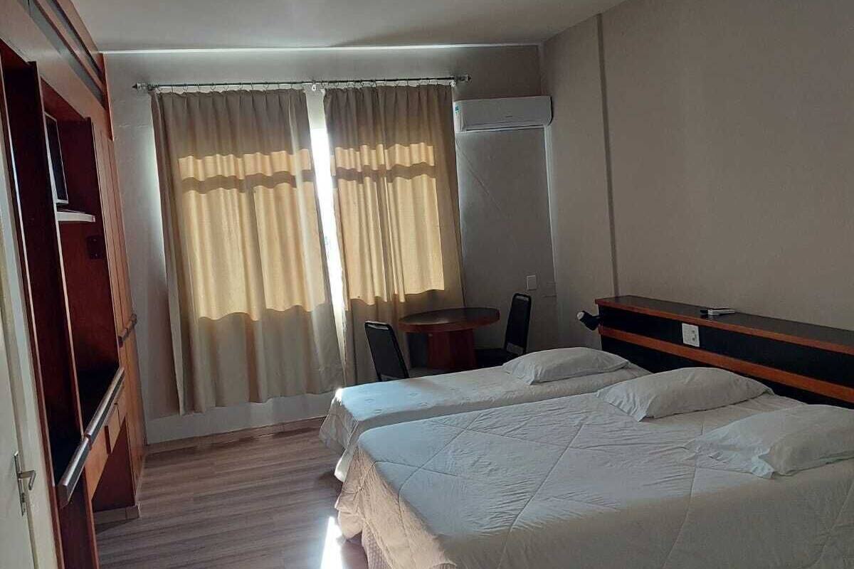 A hotel room with two beds, a desk, a chair, a wardrobe, and a window with curtains.
