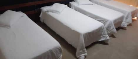 A hotel room with four single beds aligned against a wall, each with a wooden headboard and white bedding.
