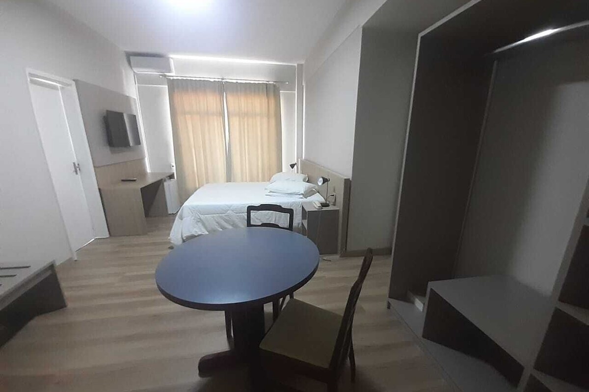 A hotel room with a bed, a round table, a chair, a TV, and a wardrobe.