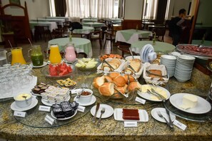 A buffet with various food items and drinks, including fruits, breads, and desserts, arranged on a granite counter.