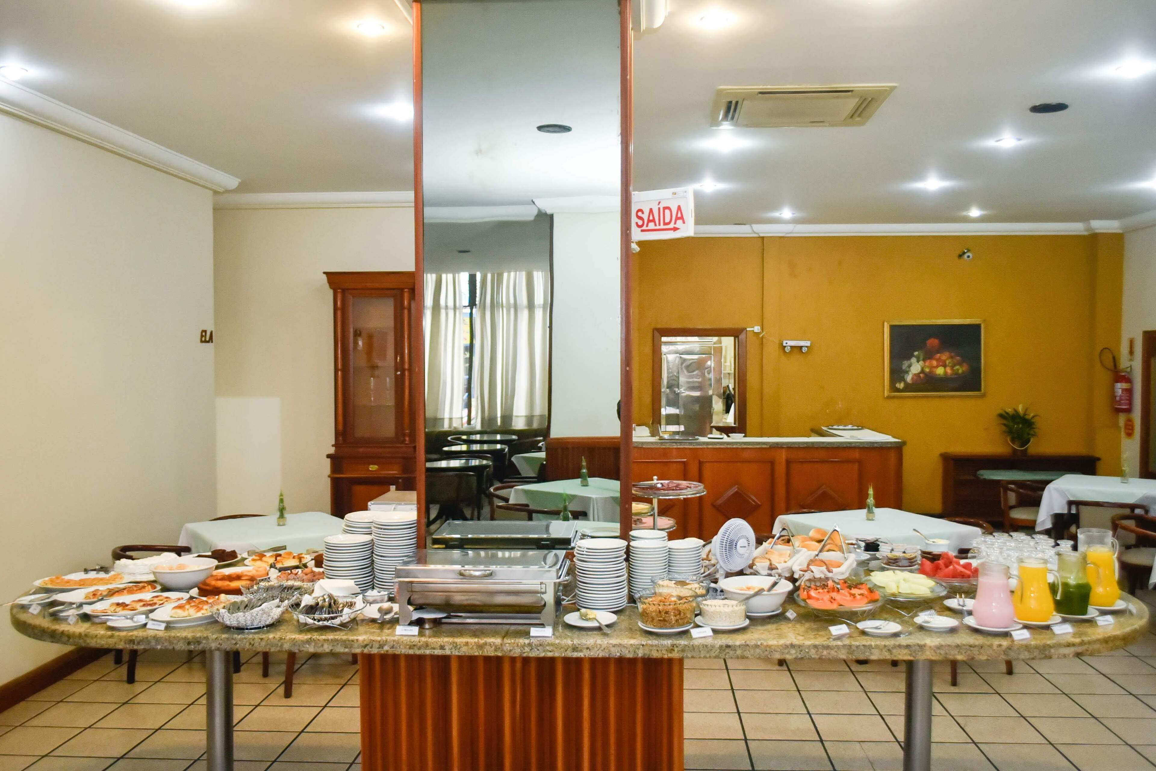 Een buffetopstelling met diverse gerechten en drankjes, een 'SAÍDA' bord en een eetgedeelte op de achtergrond.
