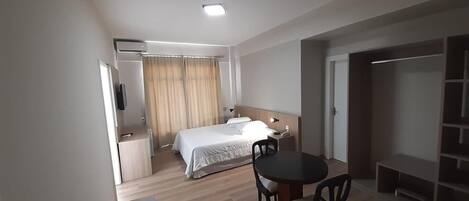 Una habitación de hotel con cama, escritorio, silla, televisor y armario.