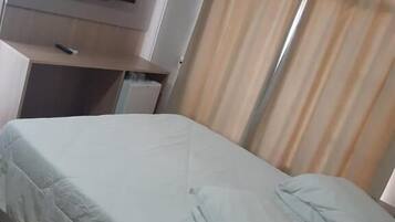 A hotel room with a bed, a TV mounted on the wall, and a window with curtains.