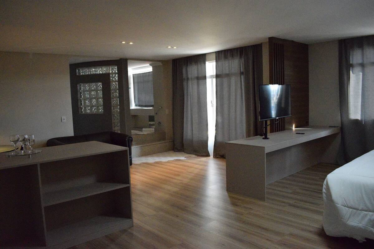 A modern hotel room with a wooden floor, a flat-screen TV, a bed, a desk, and a built-in shelf.