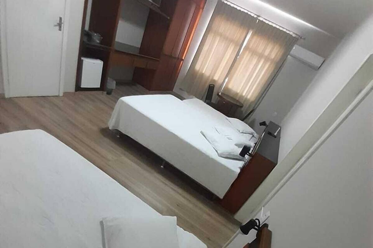 A hotel room with a bed, a small bedside table, a mirror, and a window with curtains.