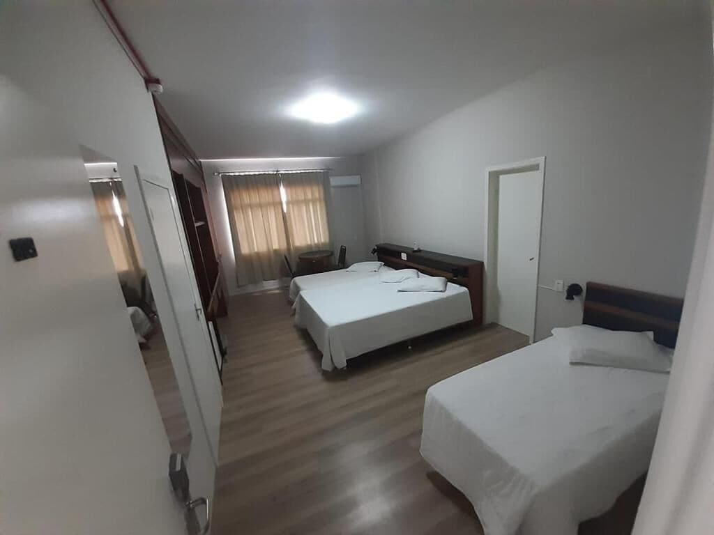 Une chambre d’hôtel avec deux lits, un plancher en bois, une porte et une fenêtre avec des rideaux.