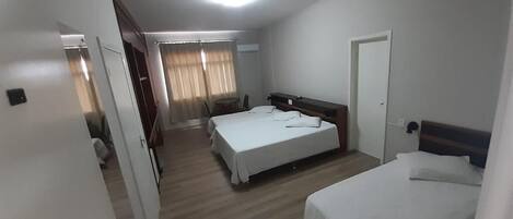 A hotel room with two beds, a wooden floor, a door, and a window with curtains.