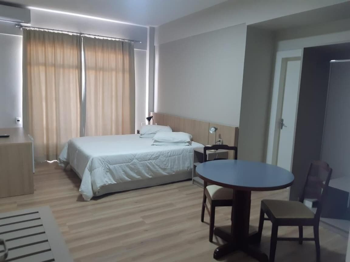 A hotel room with a bed, bedside table, lamp, and a round dining table with chairs.