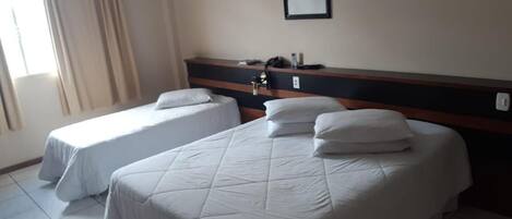 A hotel room with two beds, a headboard, a bedside table, a framed picture on the wall, and a window with curtains.