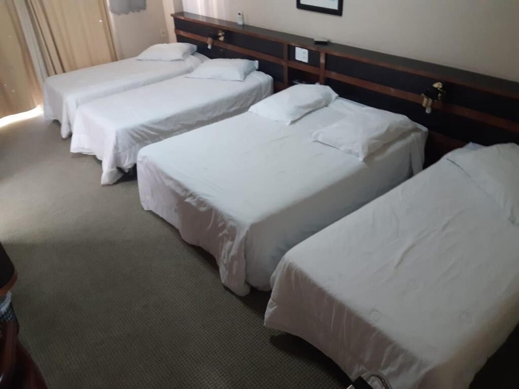 A hotel room with four single beds aligned against a wall, a wooden headboard, and a carpeted floor.
