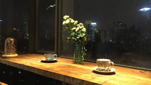 Ein Holztisch mit zwei Tassen und einer Blumenvase, einer Glaskuppel und Blick auf eine nächtliche Stadtansicht.