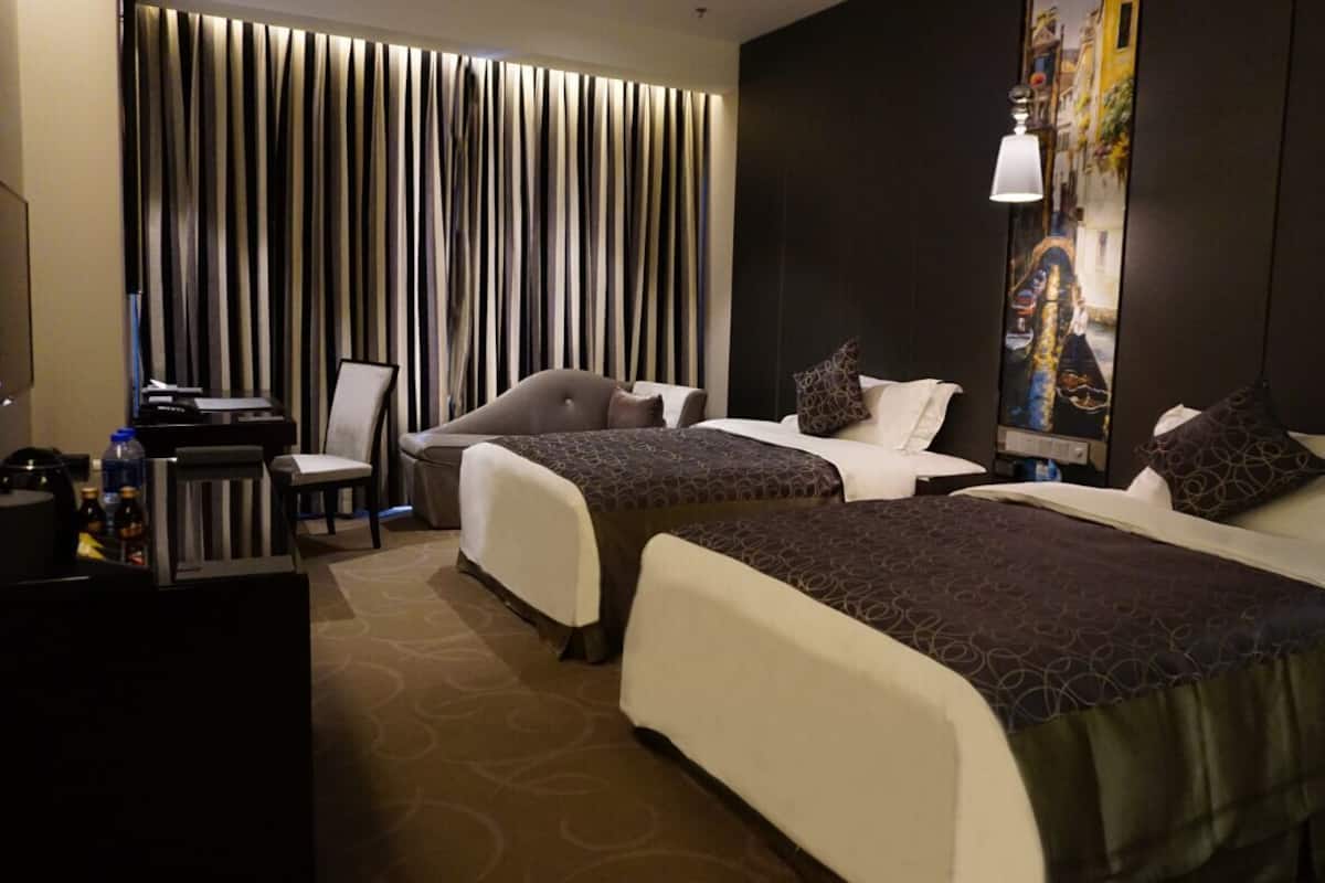 A hotel room with two beds, a desk, a chair, and a large window with curtains.