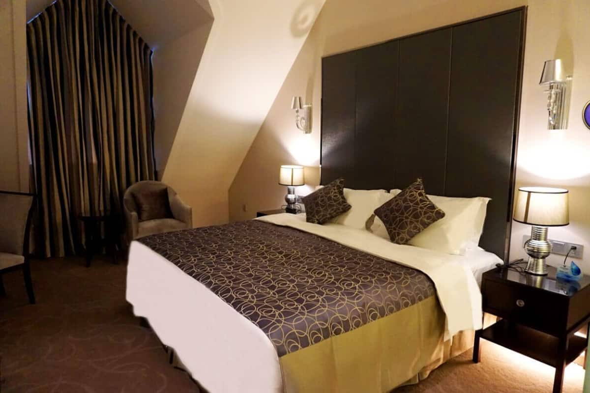 A hotel room with a large bed, two bedside tables, a chair, and a curtain.