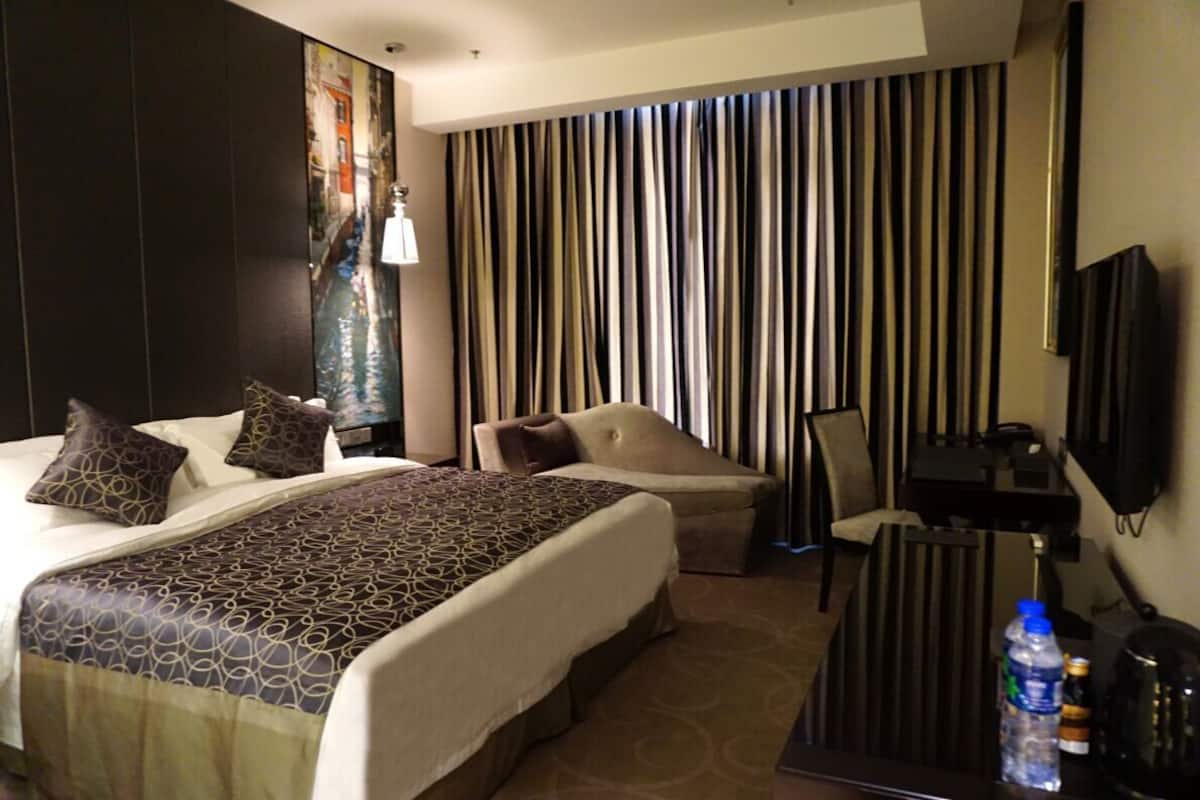A hotel room with a large bed, a desk, a chair, a TV, and a painting on the wall.