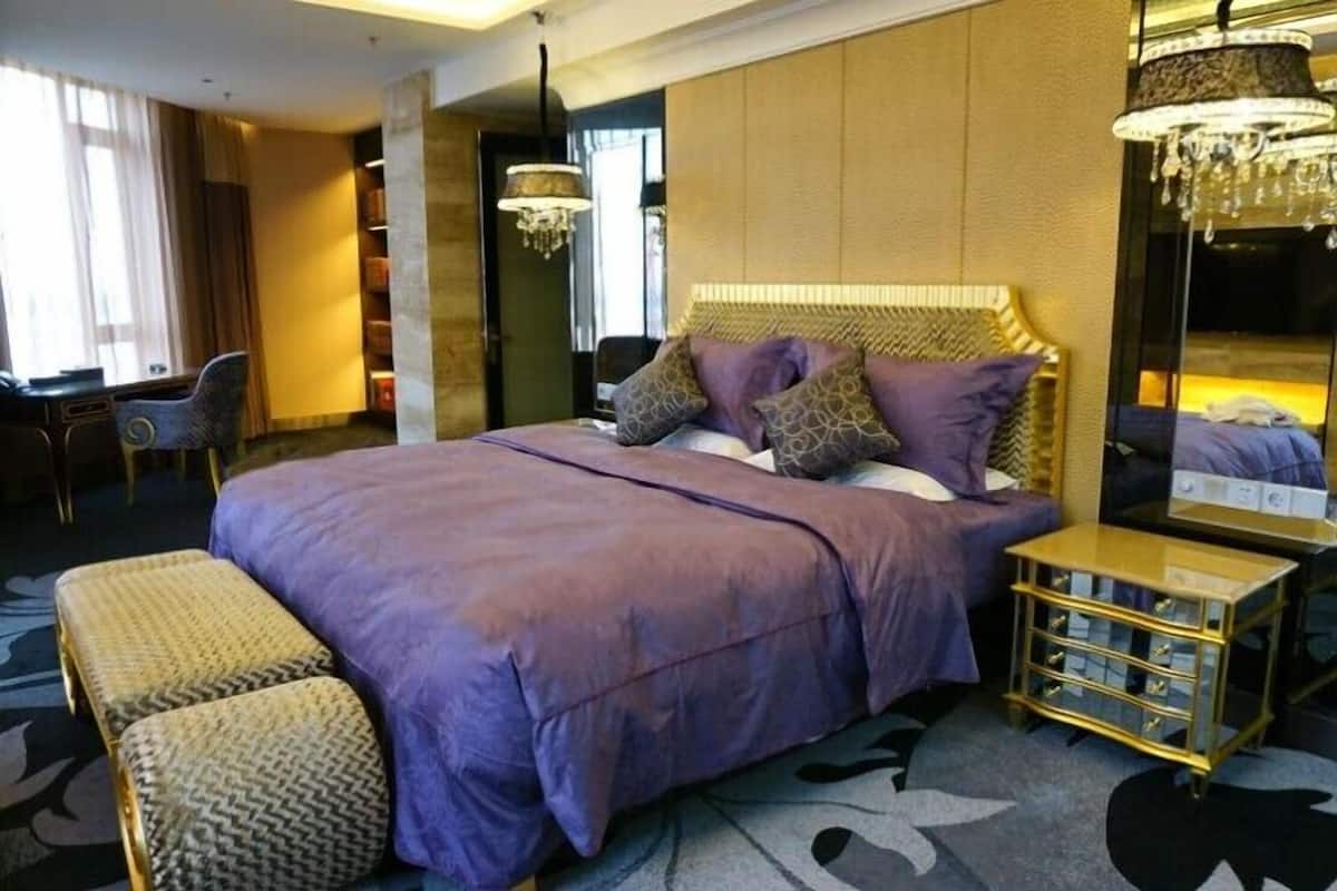 A hotel room with a large bed, a bedside table, a chair, and a mirror.
