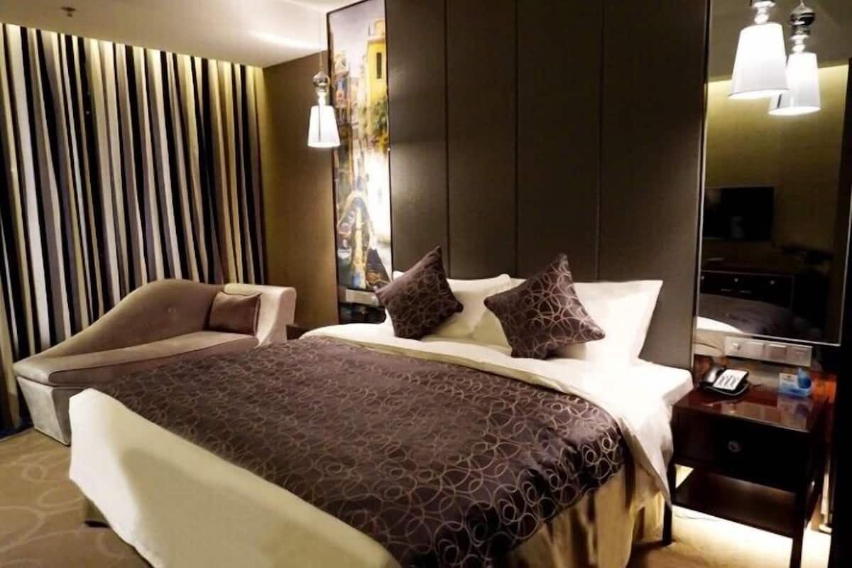 A hotel room with a bed, a sofa, a nightstand, a mirror, and a wall with vertical blinds.