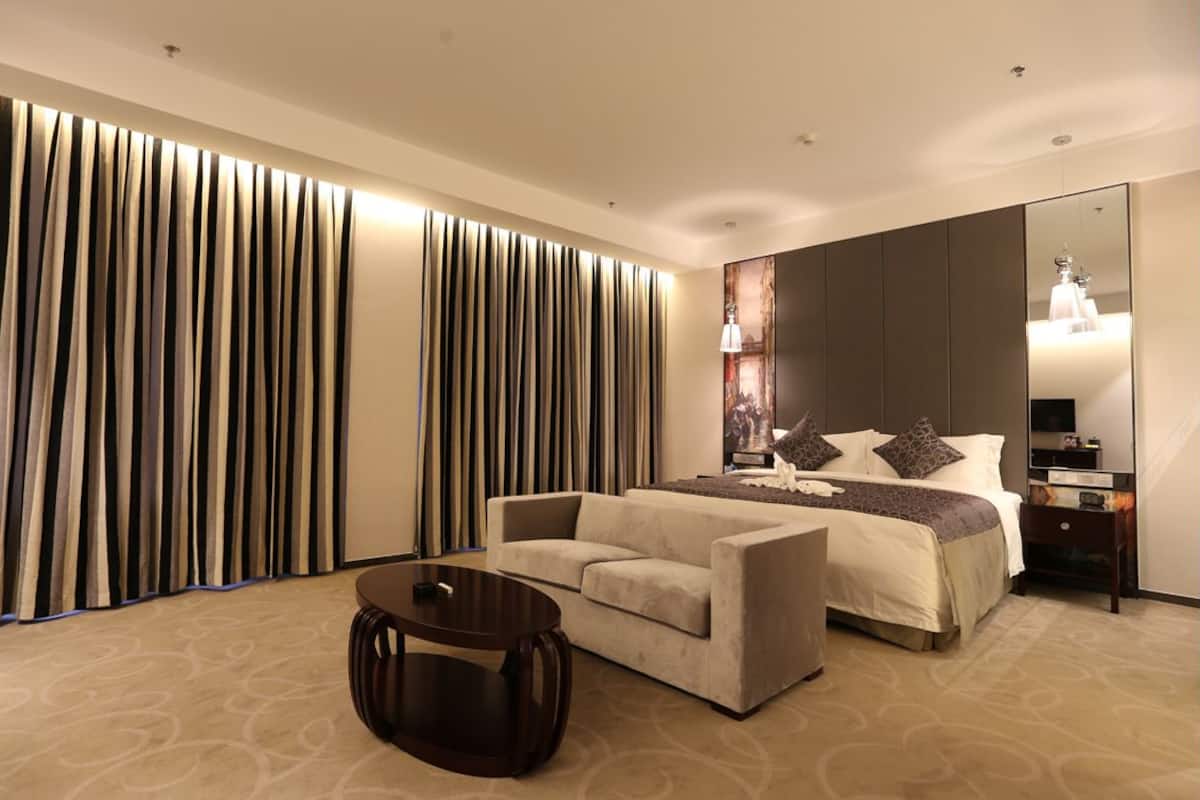 A modern hotel room with a large bed, a sofa, a round table, and a large mirror.