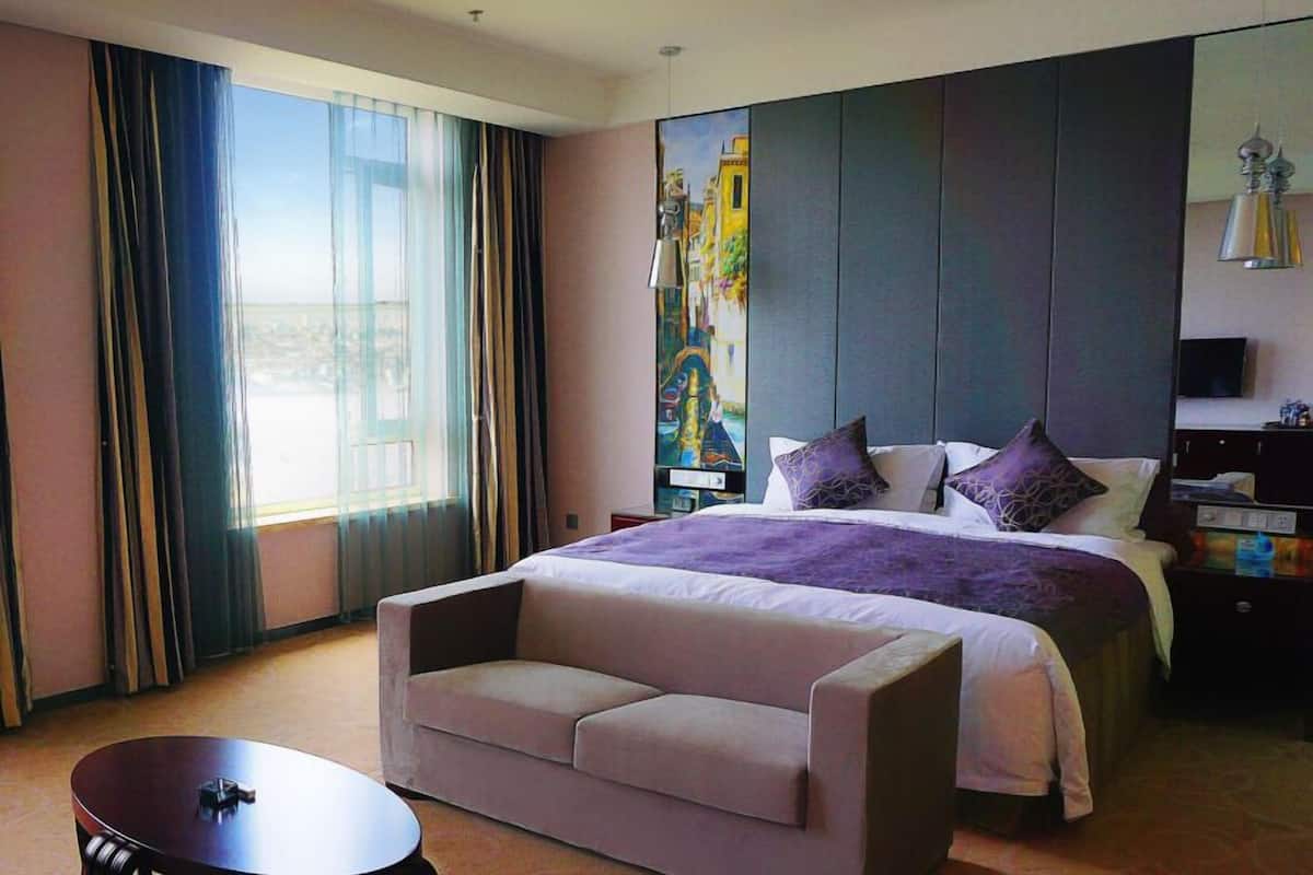 A hotel room with a large bed, a sofa, a TV, and a painting on the wall.