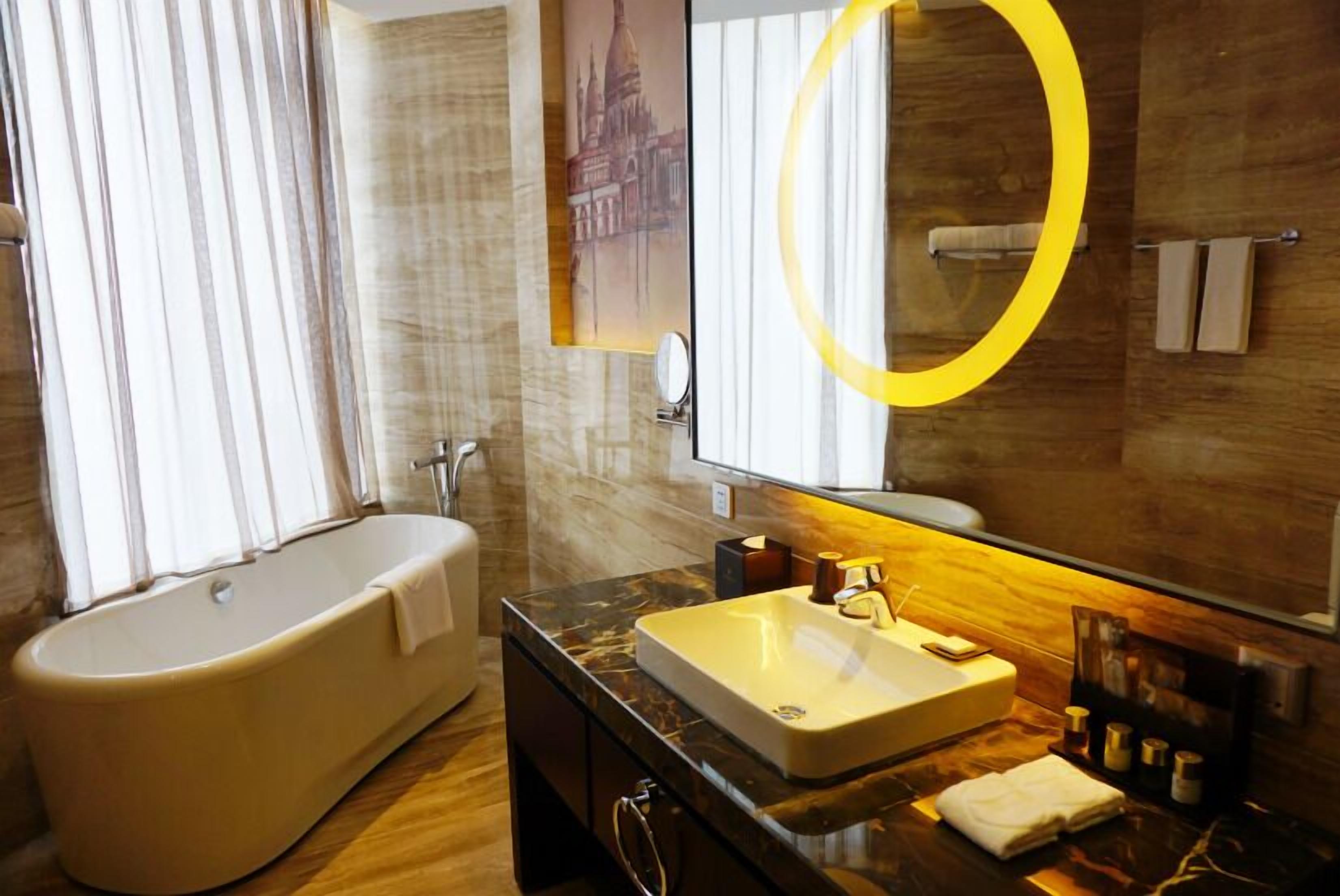 Un baño moderno con una bañera independiente, un tocador con un espejo grande y piso de madera.