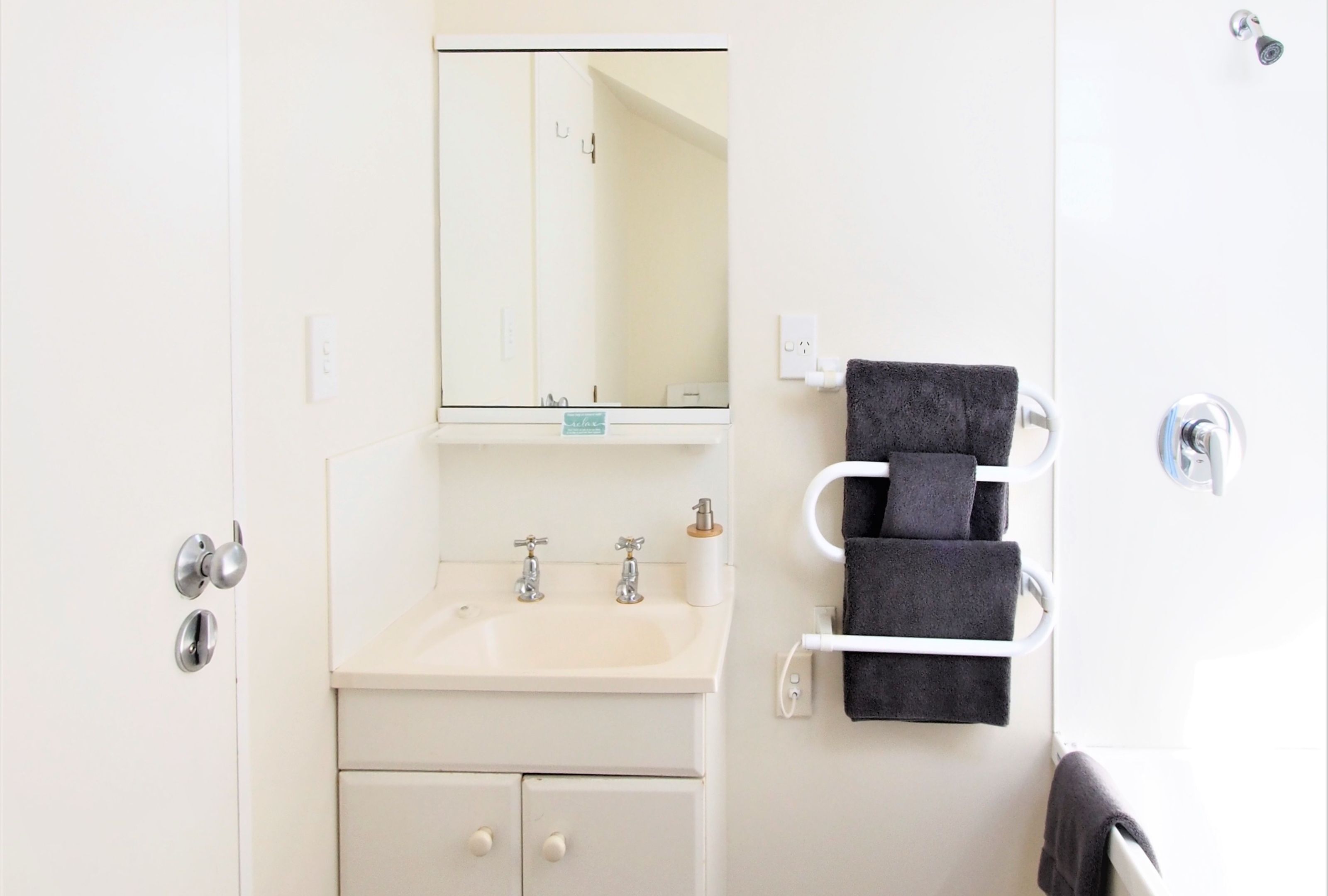 A bathroom with a white sink, two faucets, a mirror, and a towel rack with three towels.