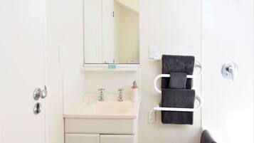 A bathroom with a white sink, two faucets, a mirror, and a towel rack with three towels.