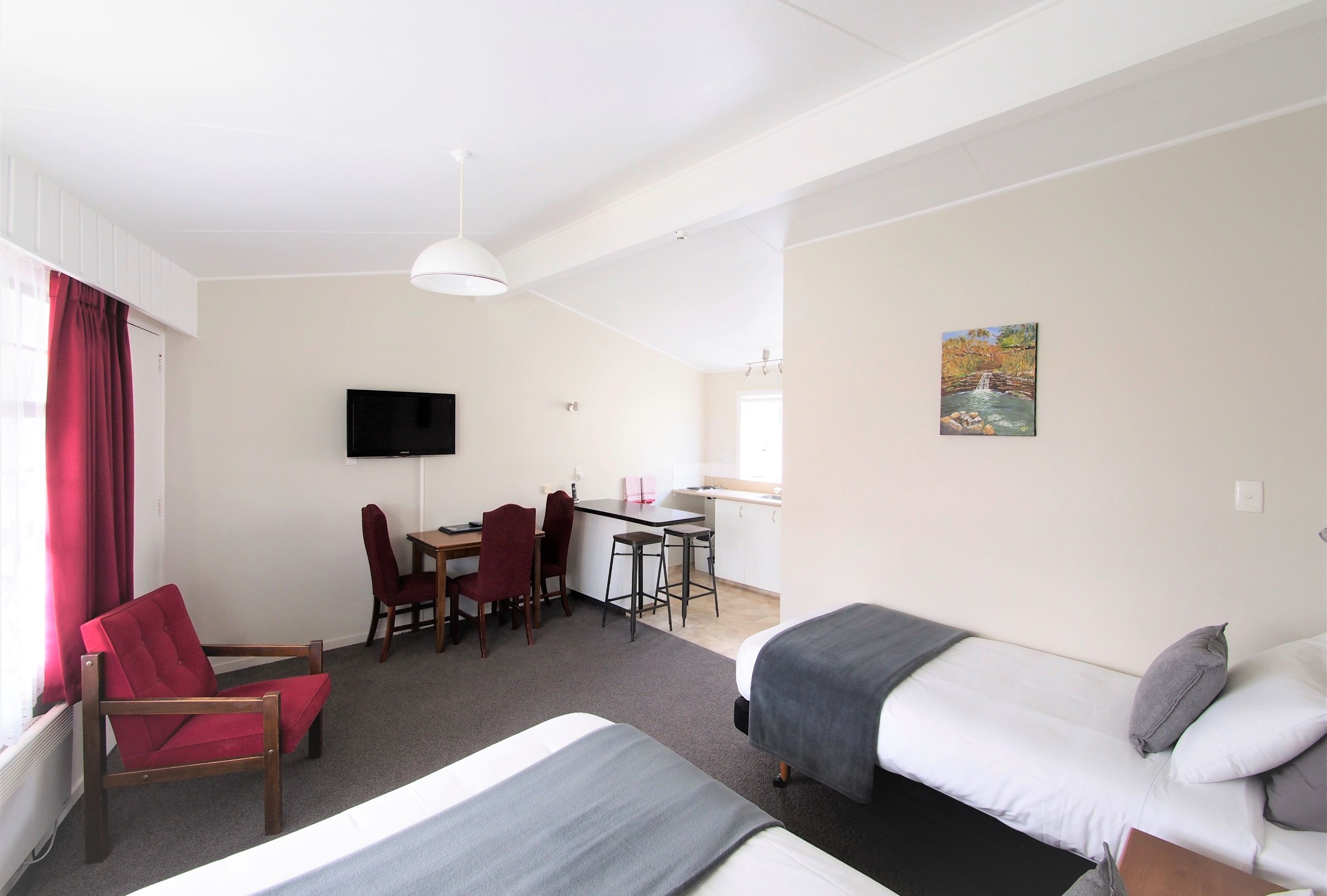 A hotel room with a bed, a desk with a chair, a TV, and a painting on the wall.