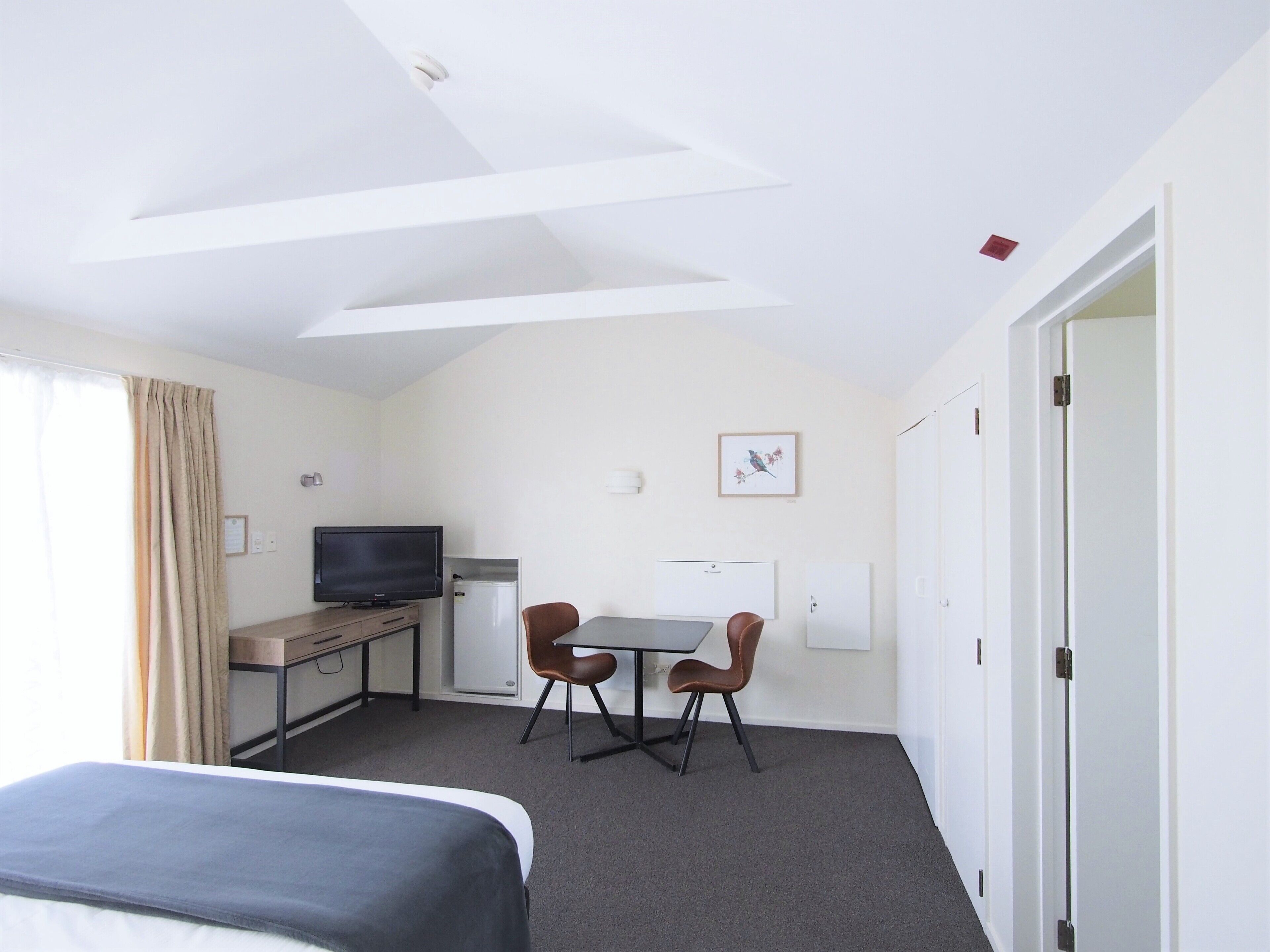Habitación de hotel con cama, escritorio con computadora, televisor y una pequeña mesa con dos sillas.