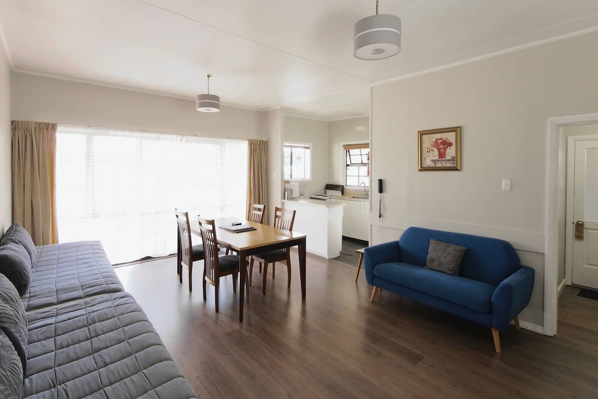 A modern living room with a dining area, a kitchen in the background, and a large window with curtains.