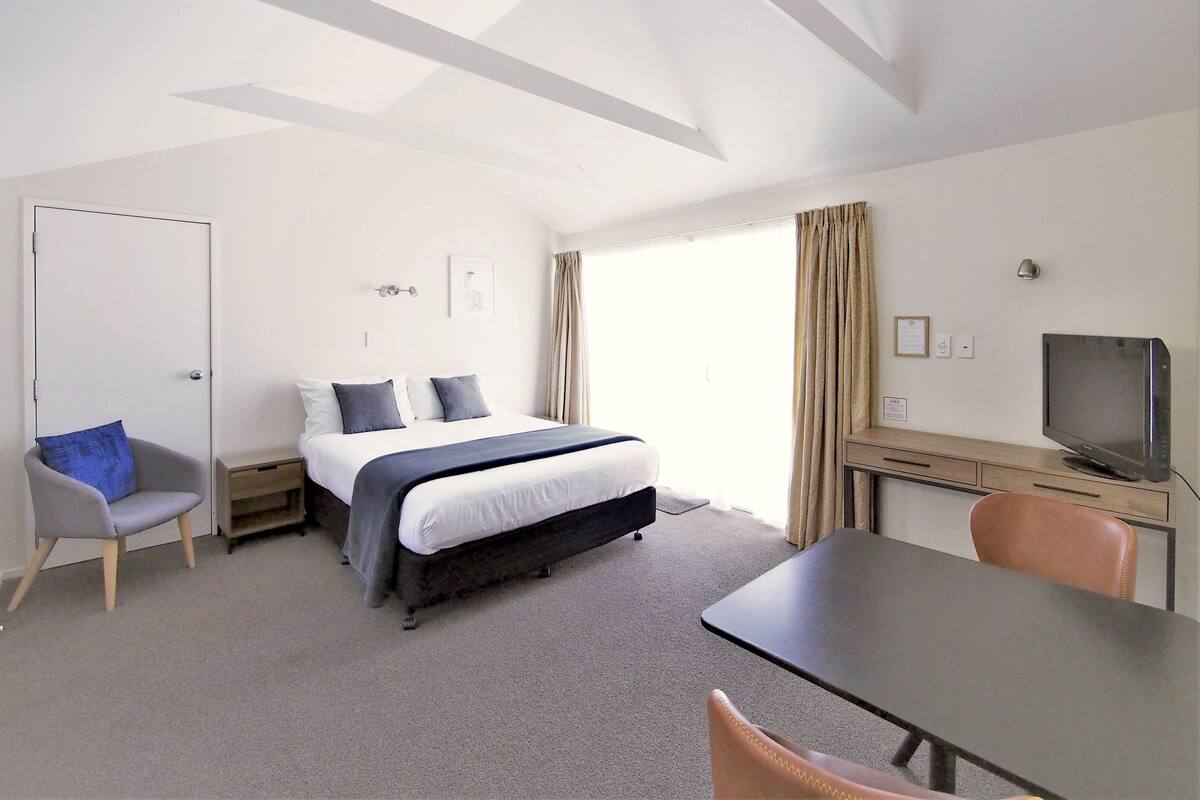 A hotel room with a bed, a desk, a chair, a television, and a door.