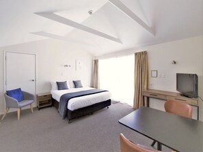 A hotel room with a bed, a desk, a chair, a television, and a door. - Riverlodge Nelson (Nelson)