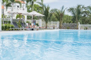A swimming pool with lounge chairs and umbrellas, surrounded by palm trees and a white fence. - Son Tra Hill Phu Quoc (Phu Quoc)