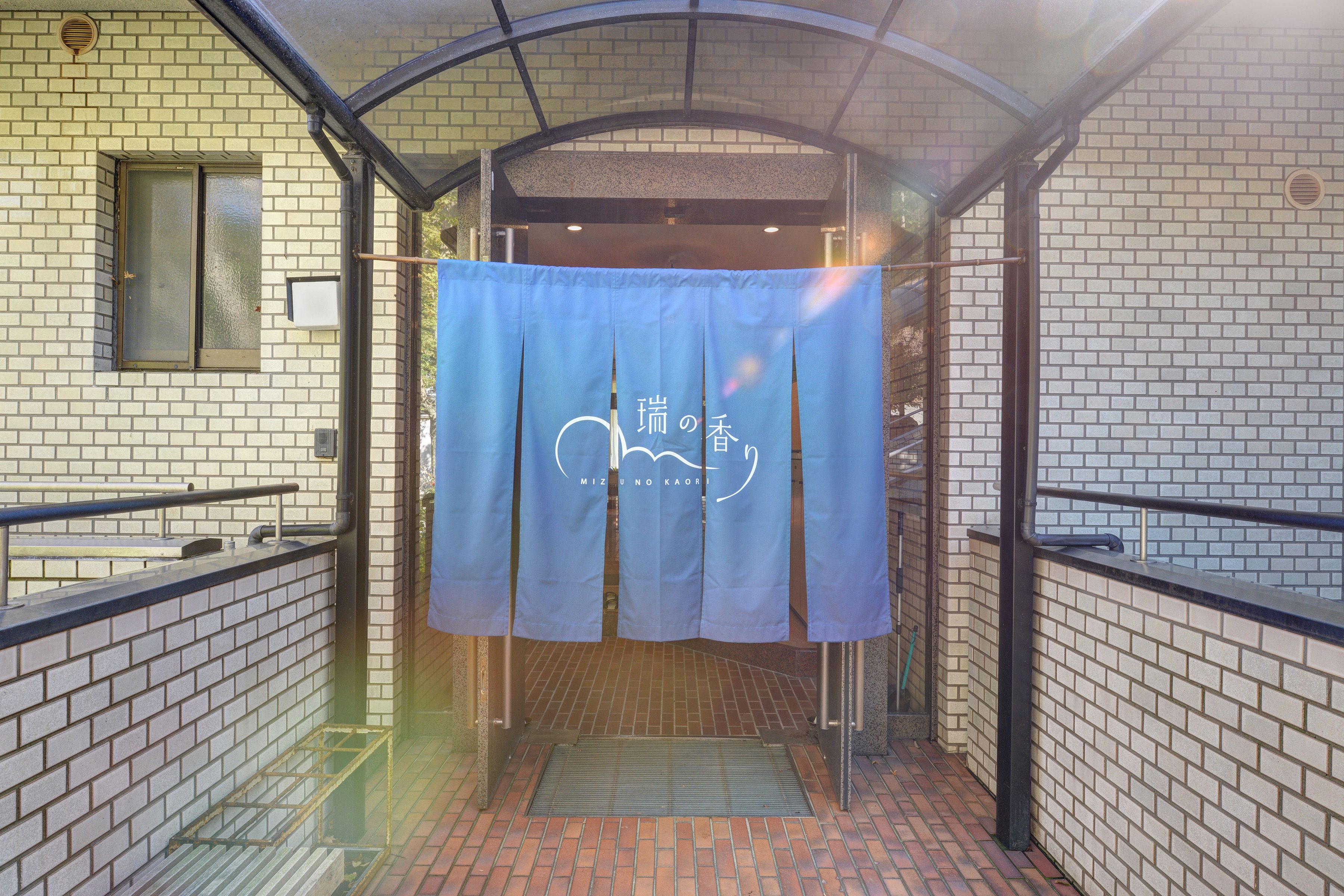 A covered entrance to a building with a tiled wall and a blue curtain with text.