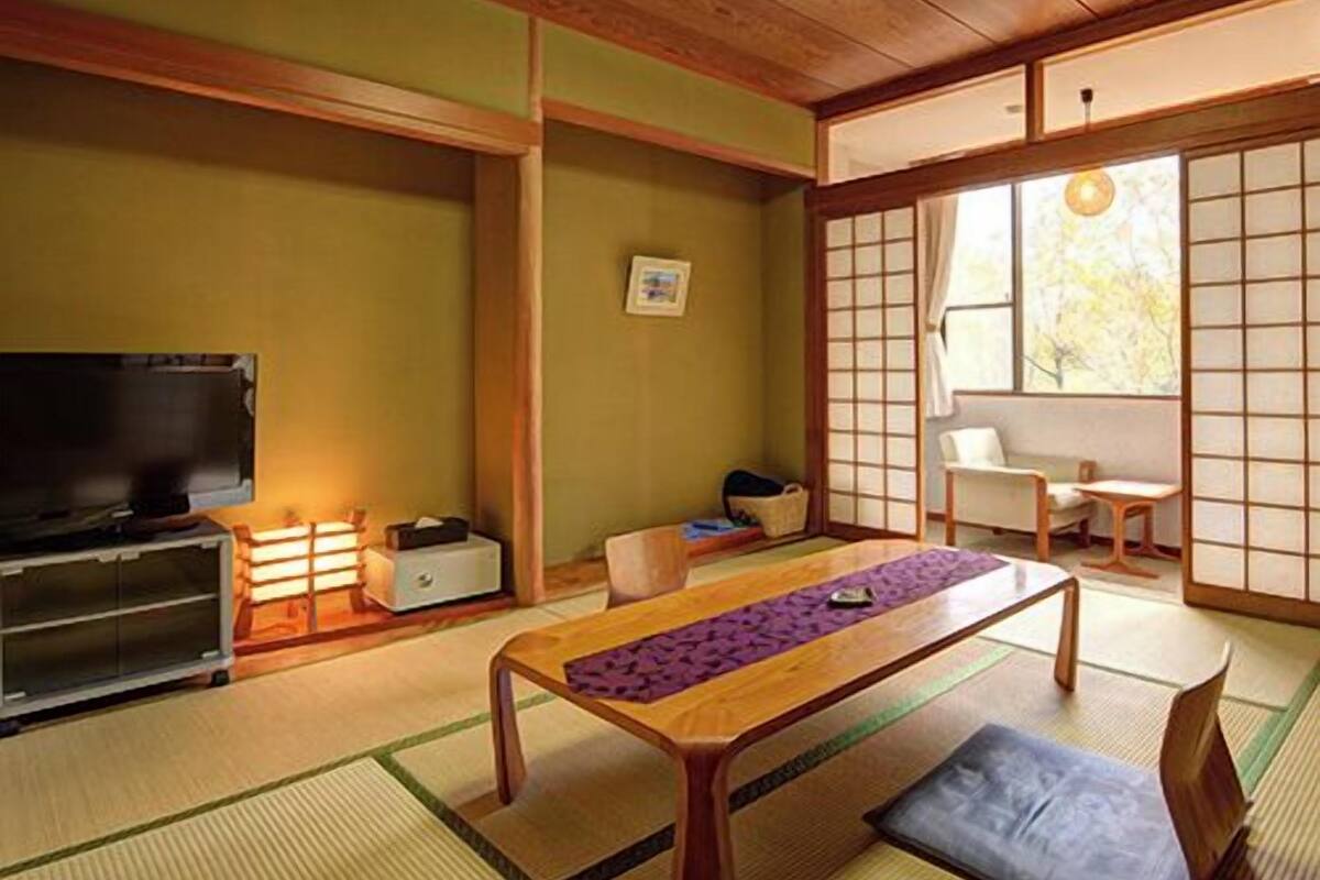 A traditional Japanese room with tatami flooring, a low wooden table, a television, and sliding doors.