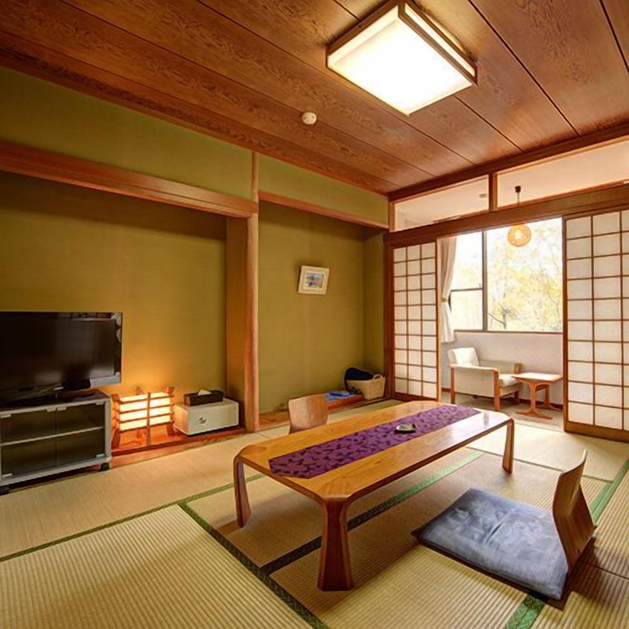 A traditional Japanese room with tatami flooring, a low wooden table, a television, and sliding doors.