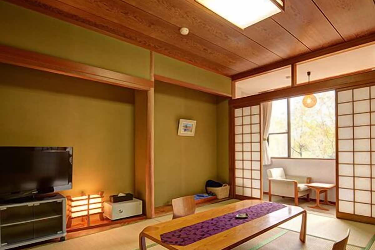 A traditional Japanese room with tatami flooring, a low wooden table, a television, and sliding doors.