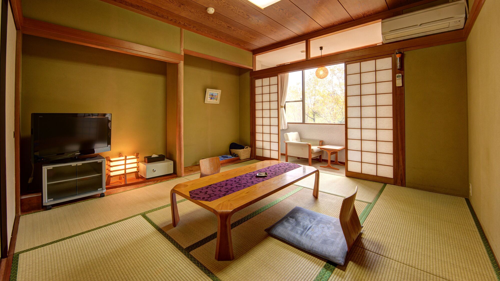 A traditional Japanese room with tatami flooring, a low table, a television, and sliding doors.