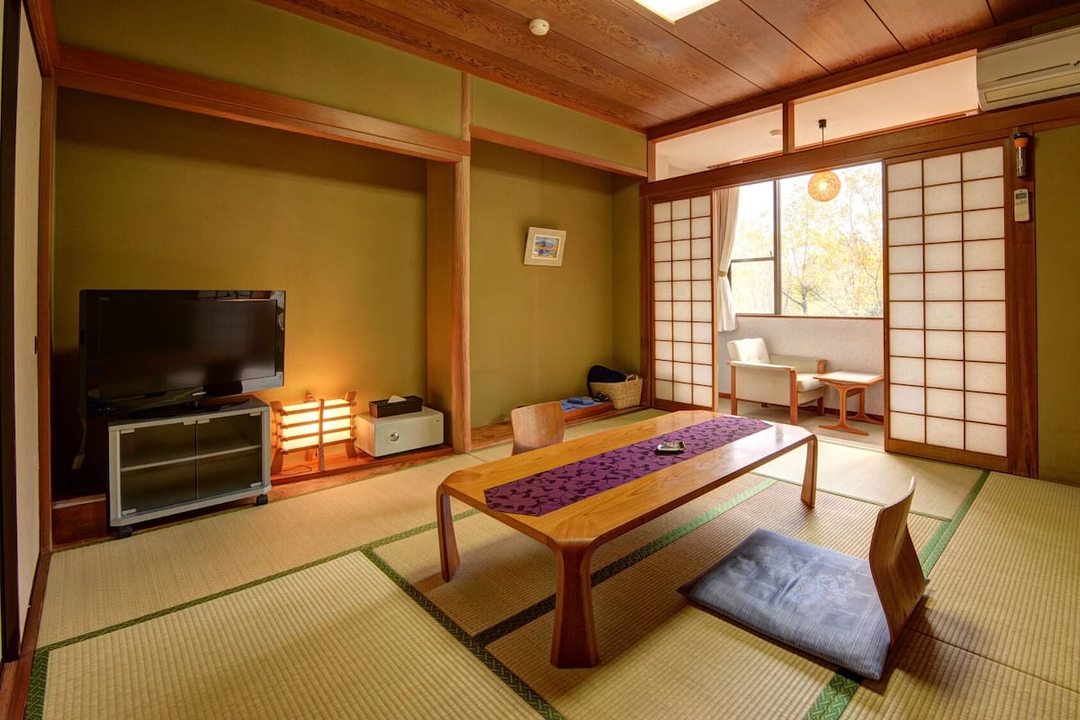 A traditional Japanese room with tatami flooring, a low table, a television, and sliding doors.