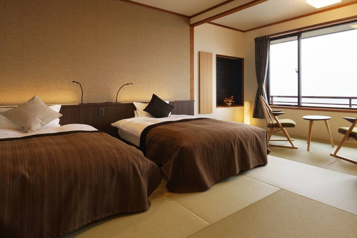 A hotel room with two beds, a desk, and a view of the outside.